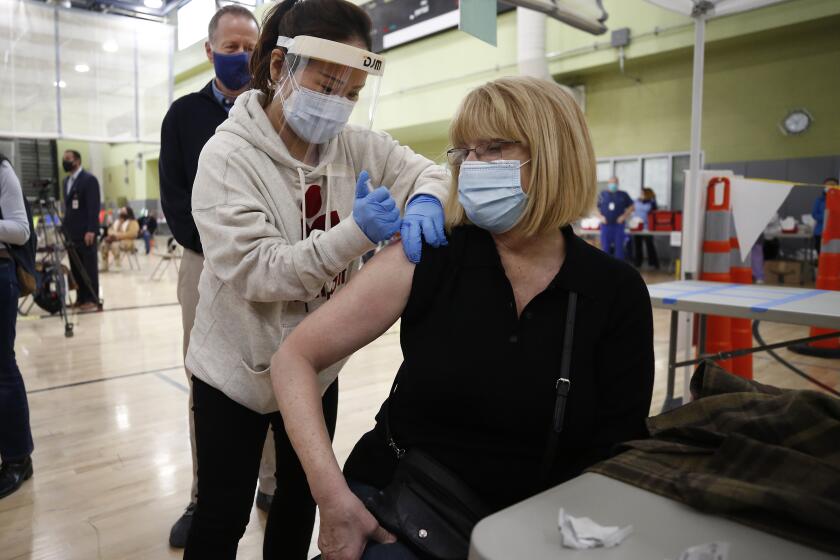 LOS ANGELES, CA - FEBRUARY 17: Pacoima Middle School teacher Abigail Abbott, 65, gets her COVID-19 vaccination from Nurse Practitioner Jiyoun Cho, left, as Los Angeles Unified employees received their first dose of the vaccine Wednesday morning. The Moderna vaccine was administered by Los Angeles Unified school nurses and other licensed healthcare professionals at the Roybal Learning Center, becoming Los Angeles Unified's first school-based vaccination center. Roybal Learning Center on Wednesday, Feb. 17, 2021 in Los Angeles, CA. (Al Seib / Los Angeles Times).