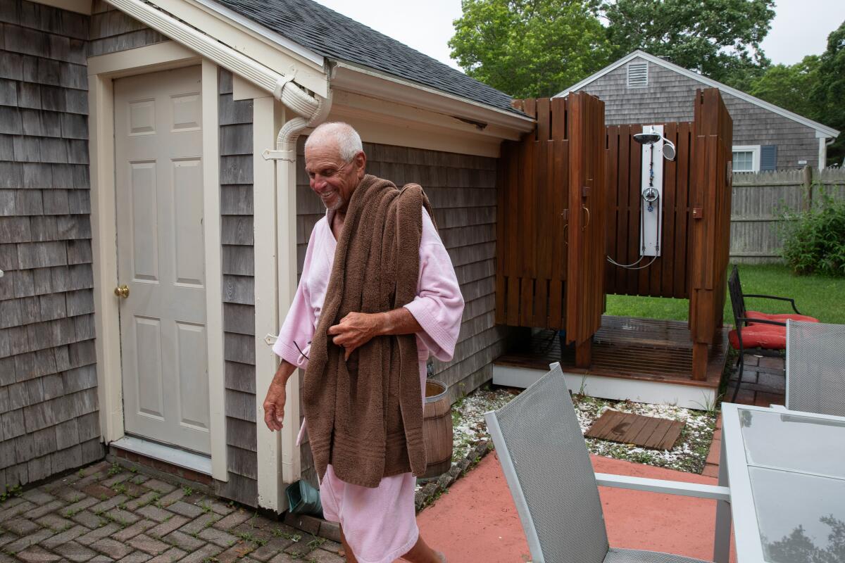 Pickler walks in a bathrobe with a towel near an outdoor shower.