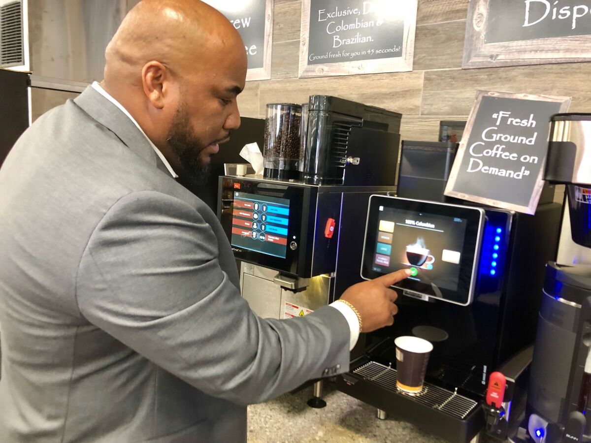 7-Eleven market manager for San Diego, Sakimo Randall, shows off one of the digital self-service cappuccino and coffee machines the company is installing at new locations to attract a wider customer base.