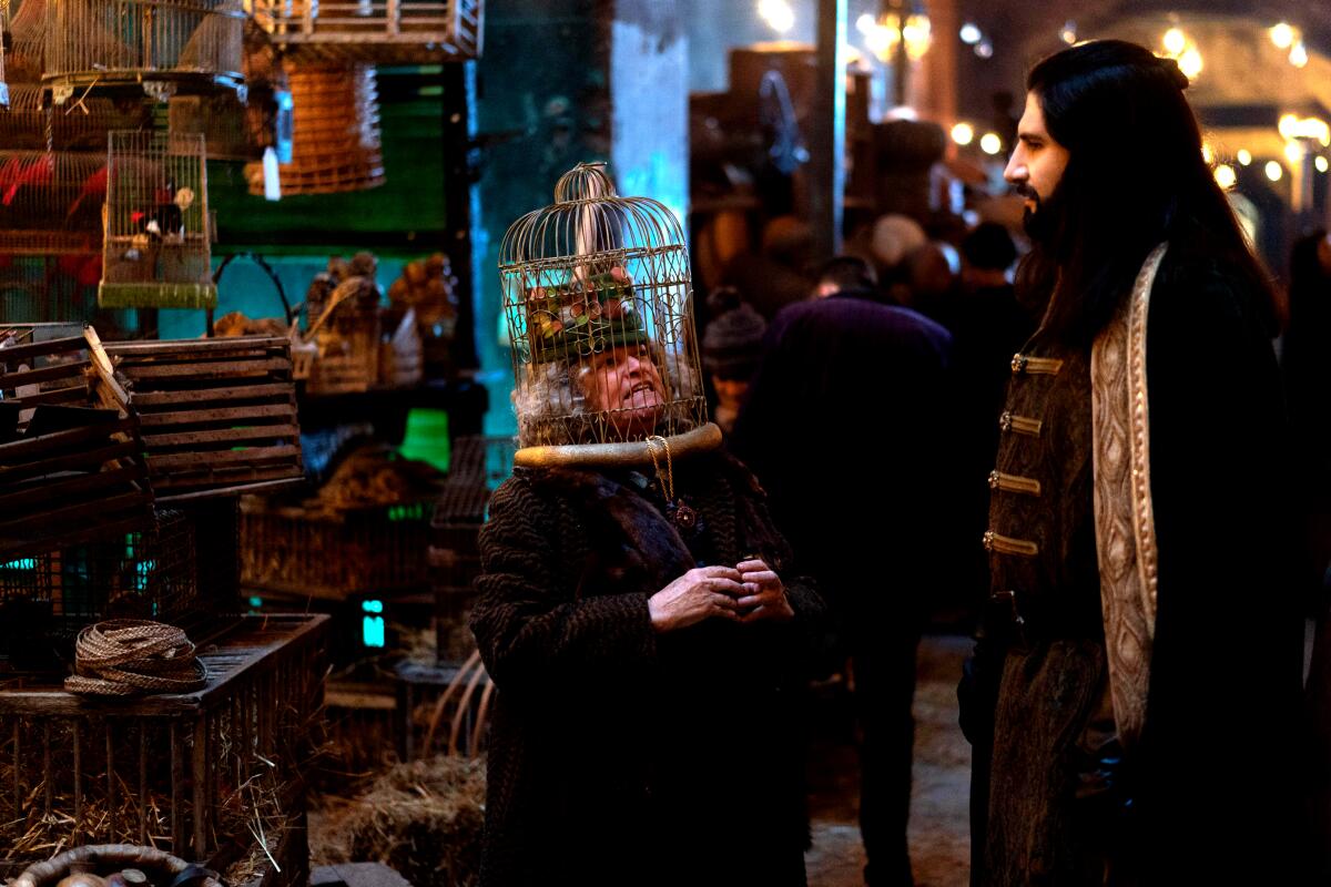 A man in ancient clothing talks to a woman with a birdcage over her head.