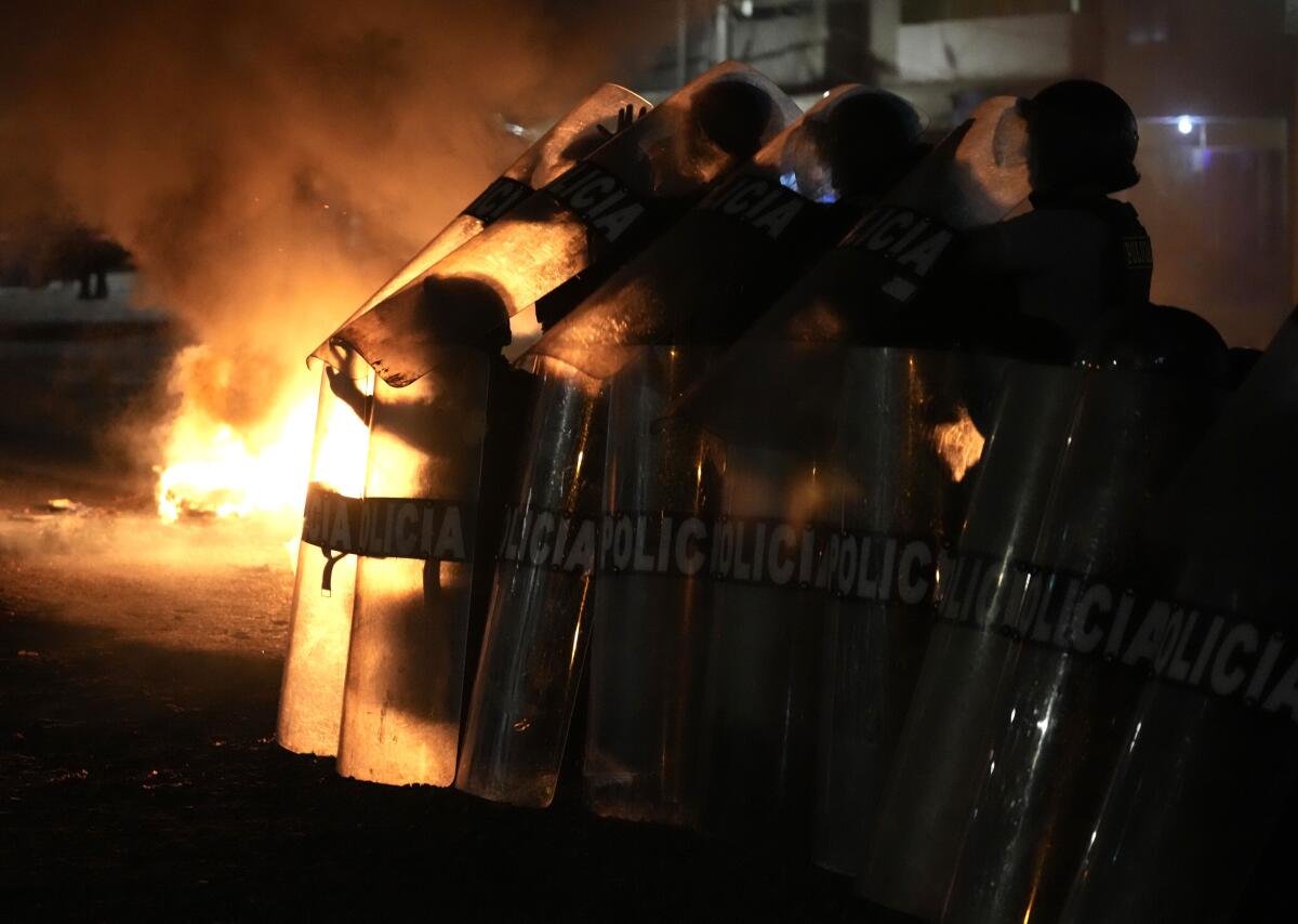 Police in riot gear silhouetted against flames.