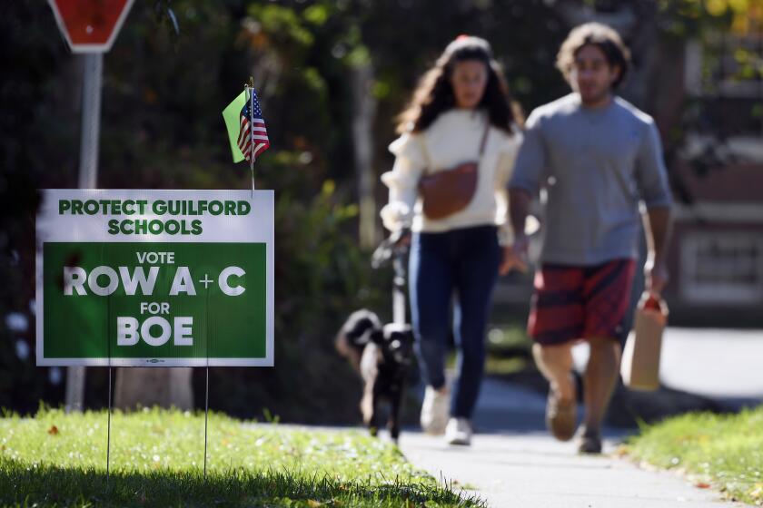 People walk near one of many signs around town centered around the upcoming Nov. 2 election and equity initiatives in schools in Guilford, Conn., on Tuesday, Oct. 19, 2021. (AP Photo/Jessica Hill)