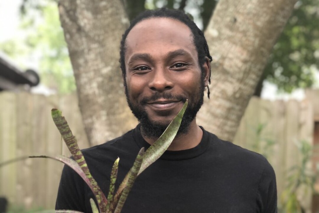 Marcus Bridgewater smiles, holding a potted plant.