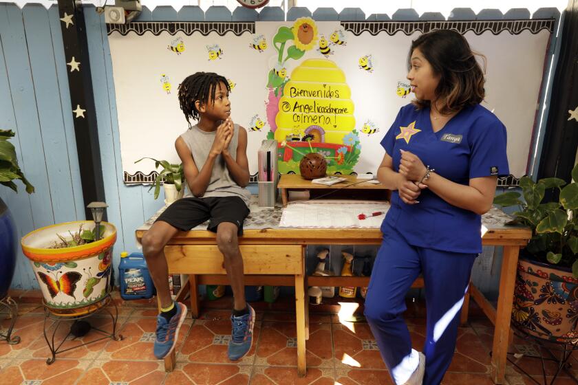 LOS ANGELES, CALIFORNIA-MARCH 25, 2020-On March 25, 2020, Tanya Garcia, age 32, right, talks to Zion Adams, 9, who has been coming to Angelica's Daycare center for many years. Tanya Garcia, age 32, runs Angelica's Daycare, a 30-year-old home daycare in Hollywood, California. The family business remains open despite the drop in clients due to the coronavirus and people remaining at home. The center went from 20 children on a normal 9 to 5 weekday, to only two. Tanya Garcia, age 32, right, talks to Zion Adams, 9, who has been coming to the center for many years. (Carolyn Cole/Los Angeles Times)