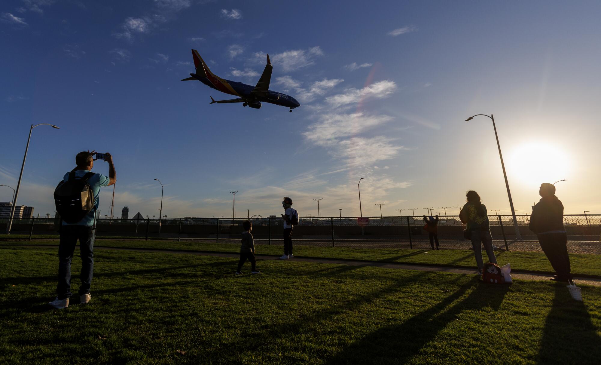 People standing on a grassy area looking at a plane coming in for a landing