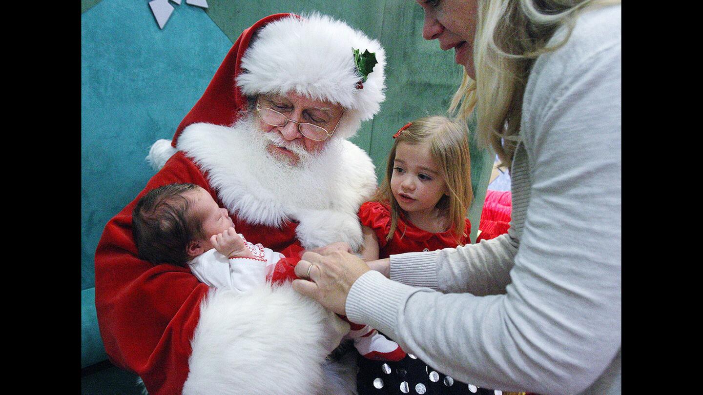 Amy Gleason, of Burbank, sets her newborn baby Paige into the arm of Santa Claus who already has daughter Rylee, 3, on his knee at the Glendale Galleria on Thursday, December 3, 2015. Worldwide Photography encourages people to sign up online for appointments to meet with Santa Claus.