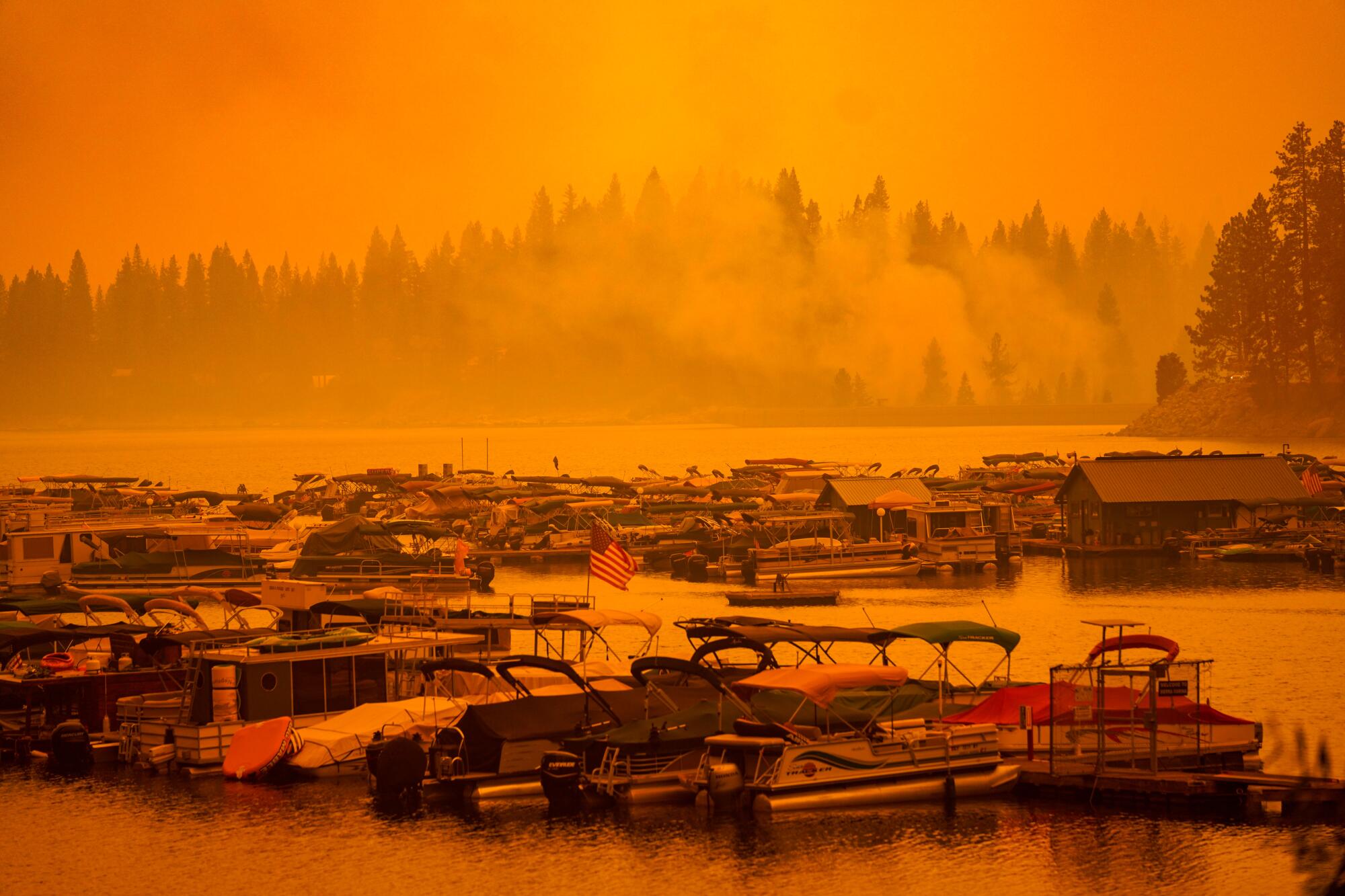 An orange haze of smoke settles over a marina of pontoon boats.
