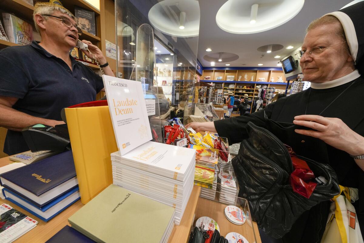 A nun faces a woman behind a counter displaying books and other items in a bookstore 