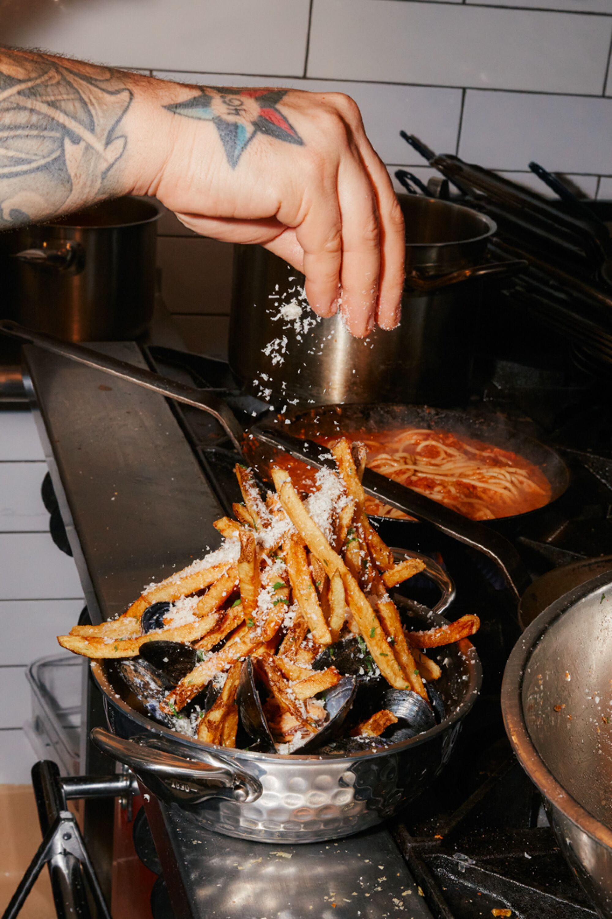 A tattooed hand sprinkles cheese over moules frites