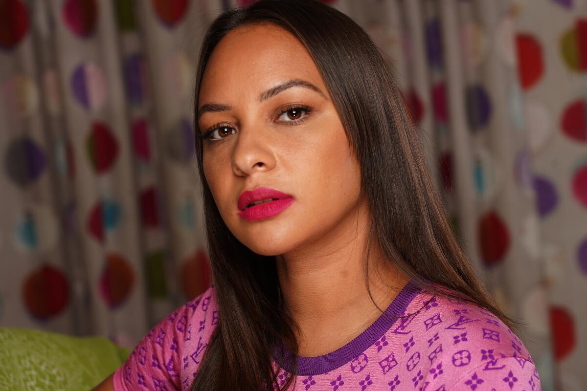 A portrait of a woman with brown hair wearing a pink shirt with Louis Vuitton print.