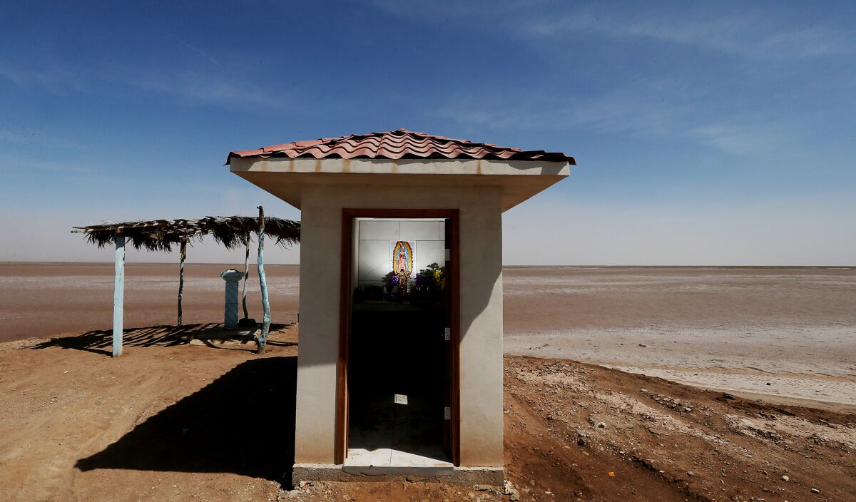 A small shrine structure with a tile roof is surrounded by miles of red dirt