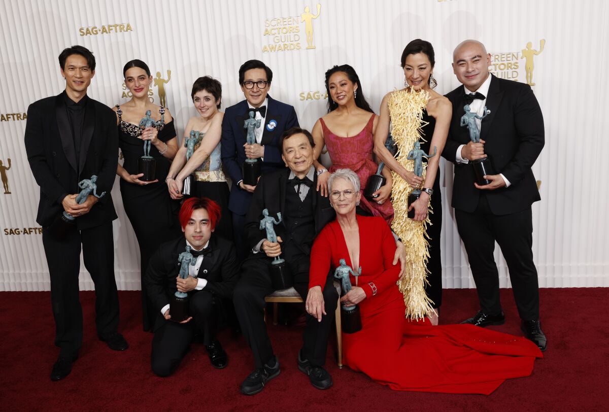 a large cast all dressed up and holding awards poses on the red carpet