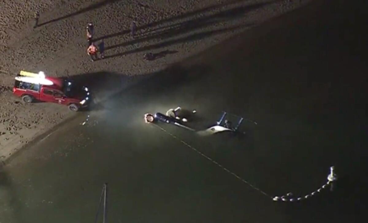 Submerged helicopter off the beach where a vehicle is parked at night with its lights on the water. 