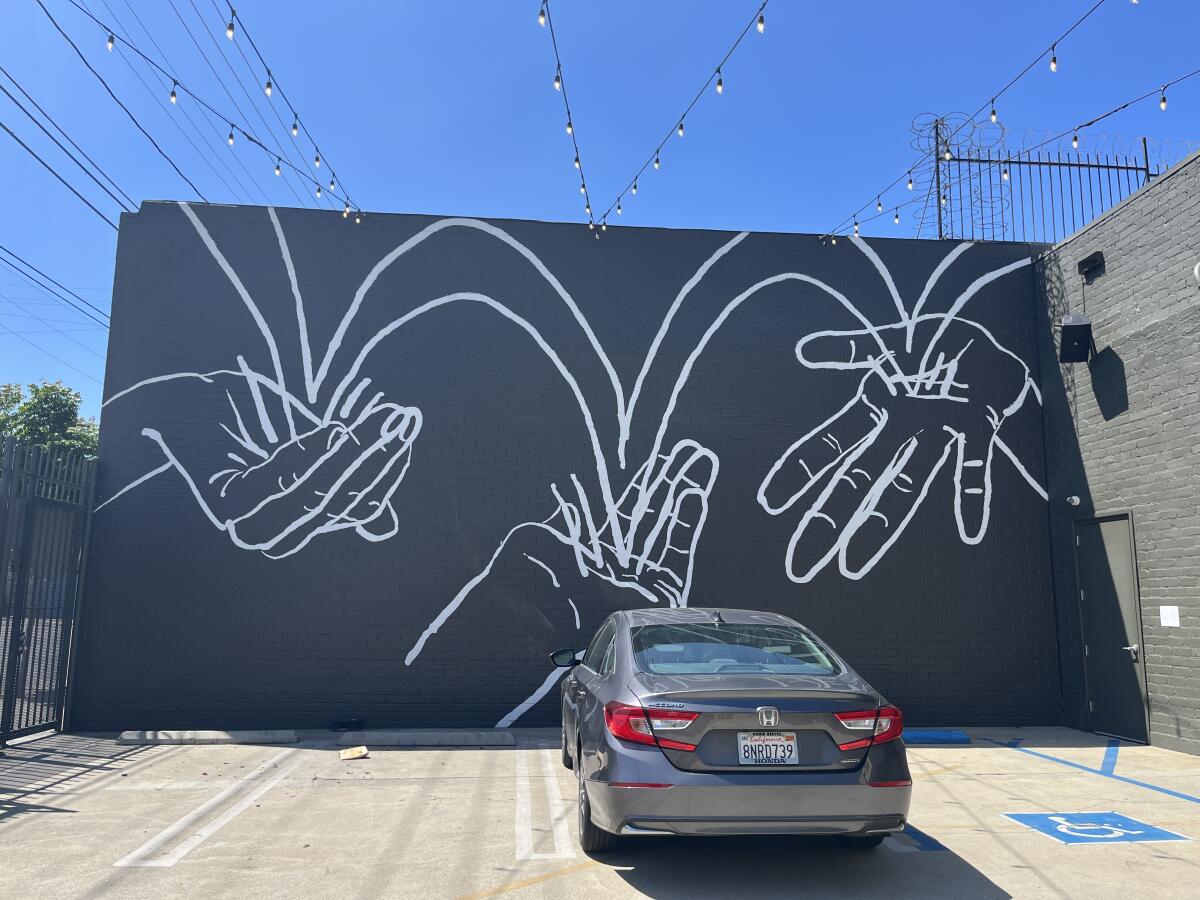 A black and white mural on a building facade shows lines bouncing between three extended hands 