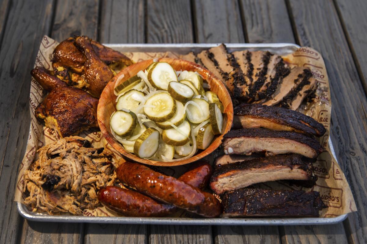 LOS ANGELES, CA - AUGUST 03: The Lunch Tray, with a bowl of homemade pickles, surrounded by, clockwise from top left, 1/2 chicken, 1/2 lb brisket, half rack of pork ribs, two Texas Red Hots and 1/2 lb pulled pork, photographed at Bludso's Bar & Que, in Los Angeles, CA, Monday, Aug. 3, 2020. The tray, which comes with a 1/2 pint of all sides, cornbread and BBQ sauce, but weren't photographed, is $90, weekday lunch only, M-F, 11:30 a.m.-3:00 p.m. (Jay L. Clendenin / Los Angeles Times)