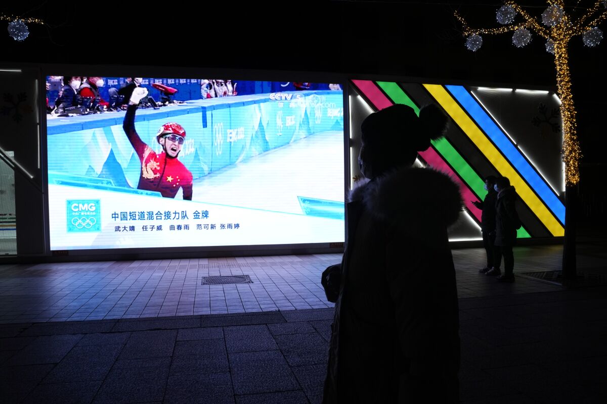 Residents watch the big screen as China's Wu Dajing celebrates after crossing the finish line to win the mixed team relay final during the short track speedskating competition to secure China's first gold medal at the 2022 Winter Olympics along a retail street in Beijing, China, Saturday, Feb. 5, 2022, in Beijing. (AP Photo/Ng Han Guan)