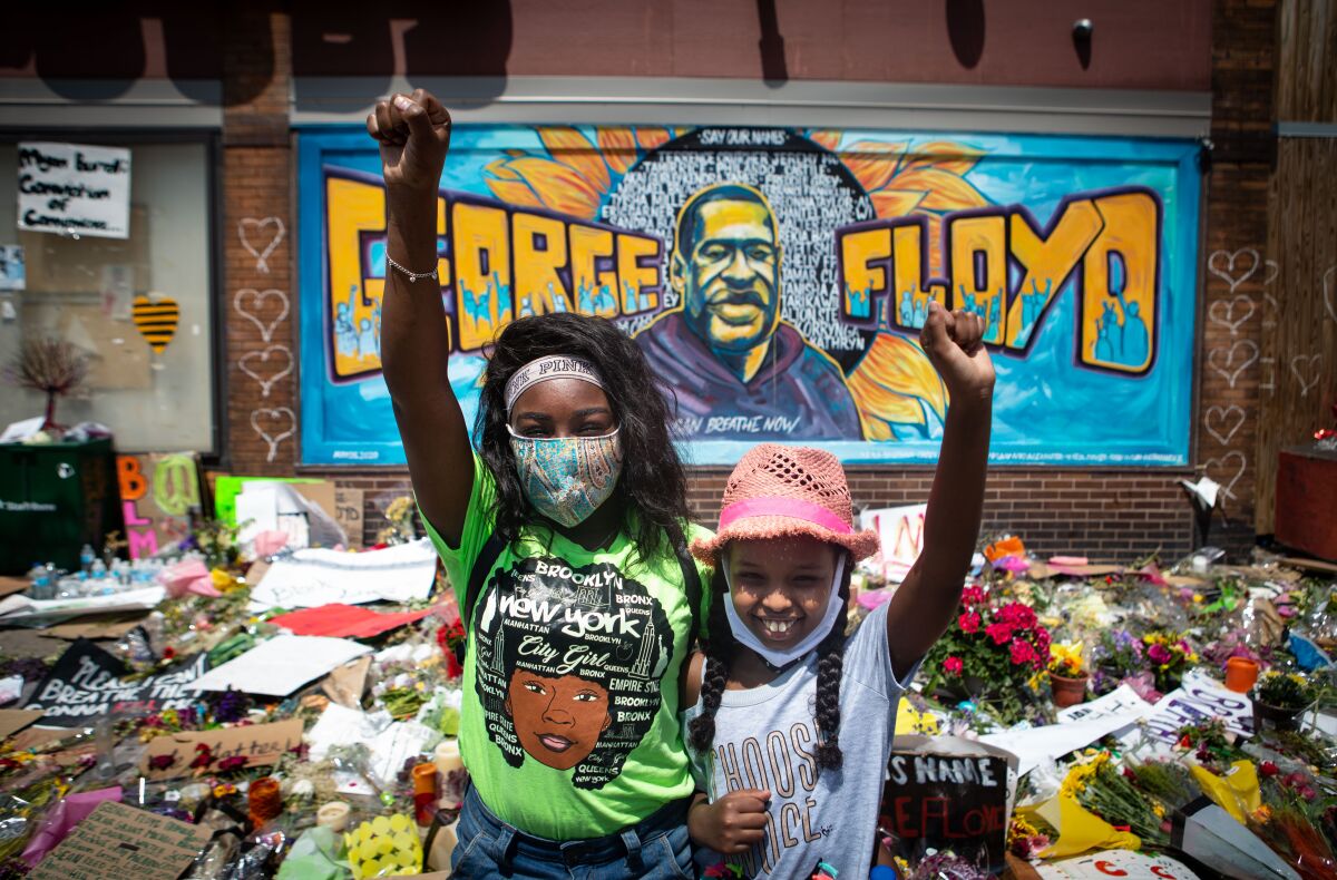 Two black girls with fists raised stand in front of makeshift memorial for George Floyd in Minneapolis.