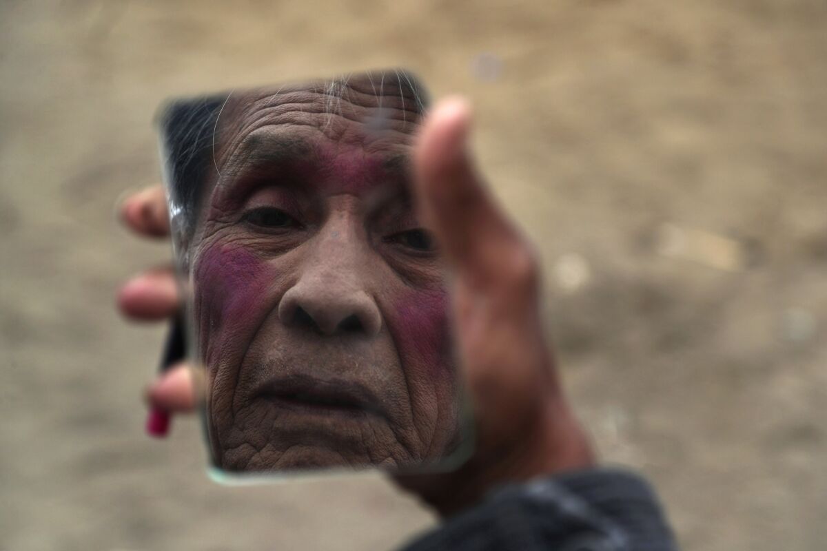 Circus clown Santos Chiroque, whose performance name is "Piojito," or Little Tick, looks into a mirror as he demonstrates how he puts on his clown makeup, using just lipstick, outside his home on the outskirts of Lima, Peru, Monday, Aug. 10, 2020. Chiroque's family used to run their own small circus, but since March when the lockdown to curb COVID-19 closed down their business, and the requirement for people over 60 to self-quarantine kept the 74-year-old at home, they started selling circus food like caramelized apples to survive. (AP Photo/Martin Mejia)