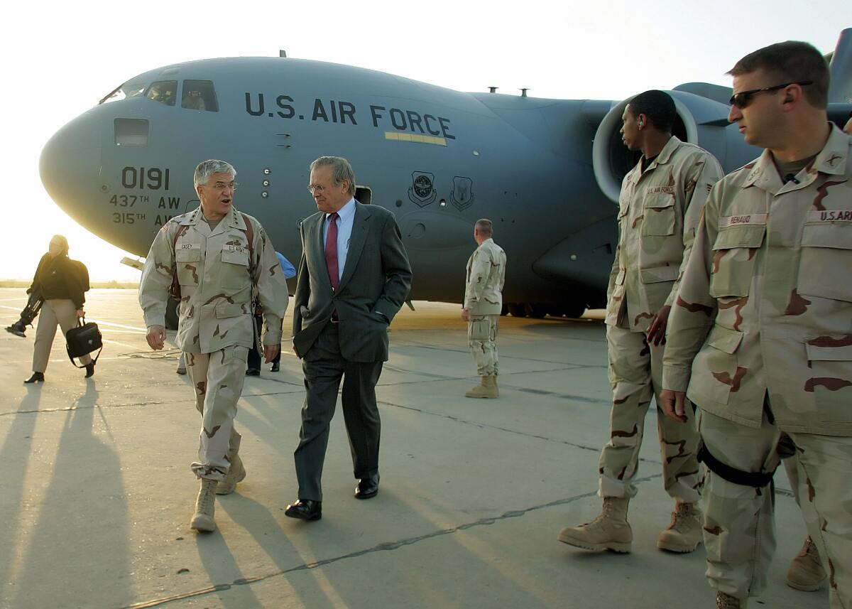 Donald H. Rumsfeld walks on an airport tarmac with a U.S. military official.