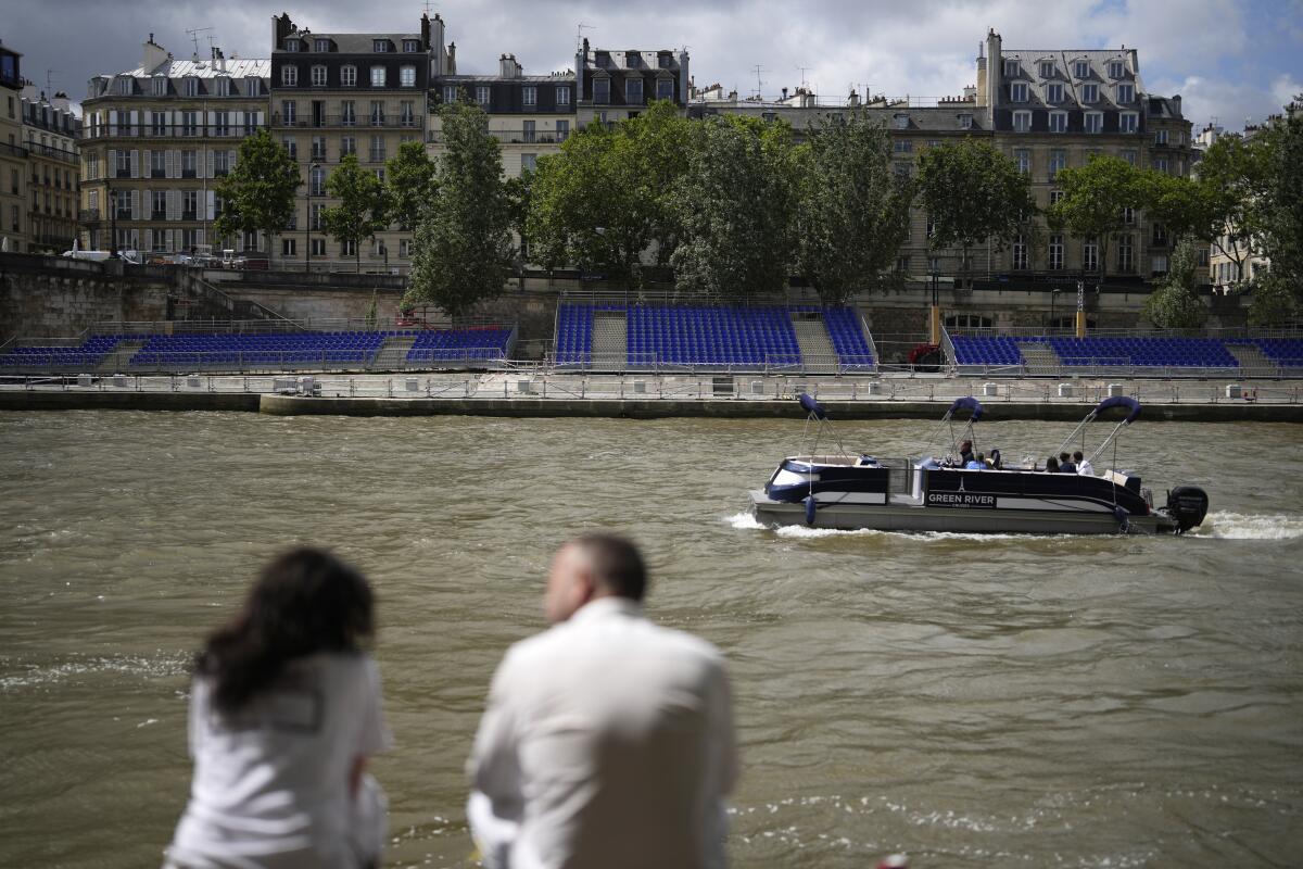 People sit along the Seine river with stands installed on its banks.
