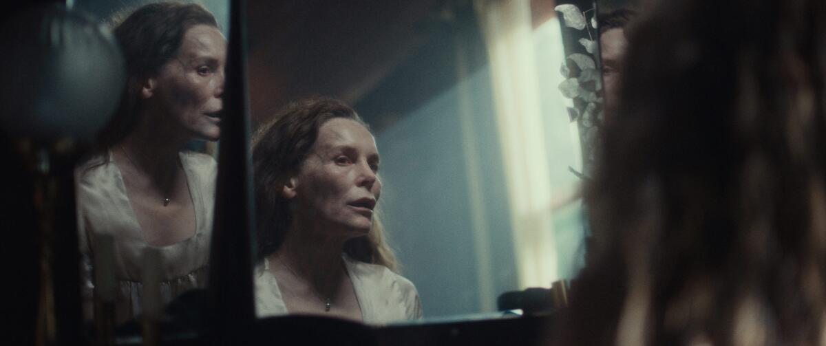 A woman looks at multiple reflections of herself in a mirror in in the movie "She Will."