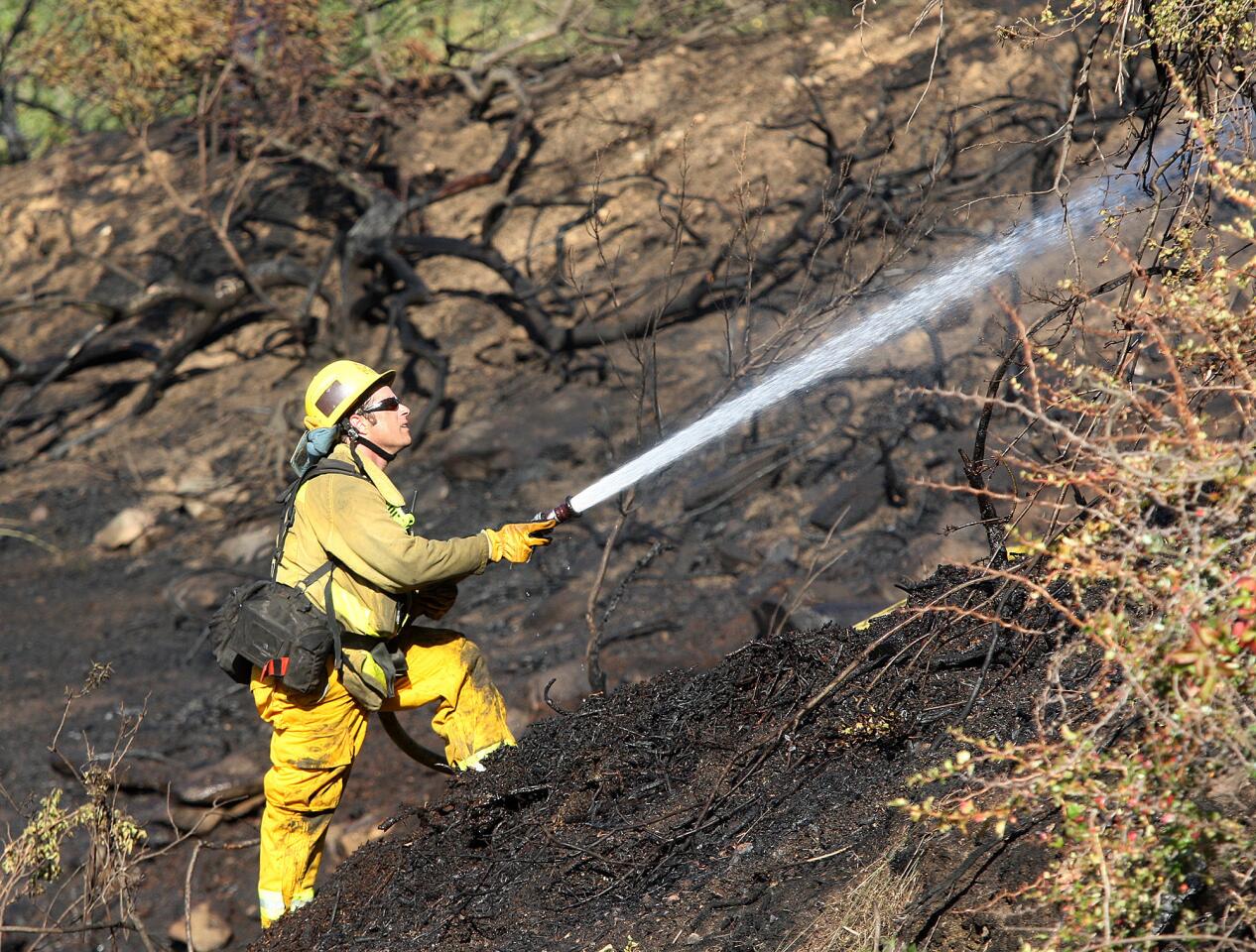 A firefighter shoots a steady steam of water onto hotspots during the mop up of a 2-acre brush fire, brought under control by fire departments from Glendale, Pasadena and Burbank on Figureroa Street in Glendale on Wednesday, June 4, 2014. The fire was on the Pasadena side of the street, but those on the Glendale side of the street were impressed with the quick response and result.