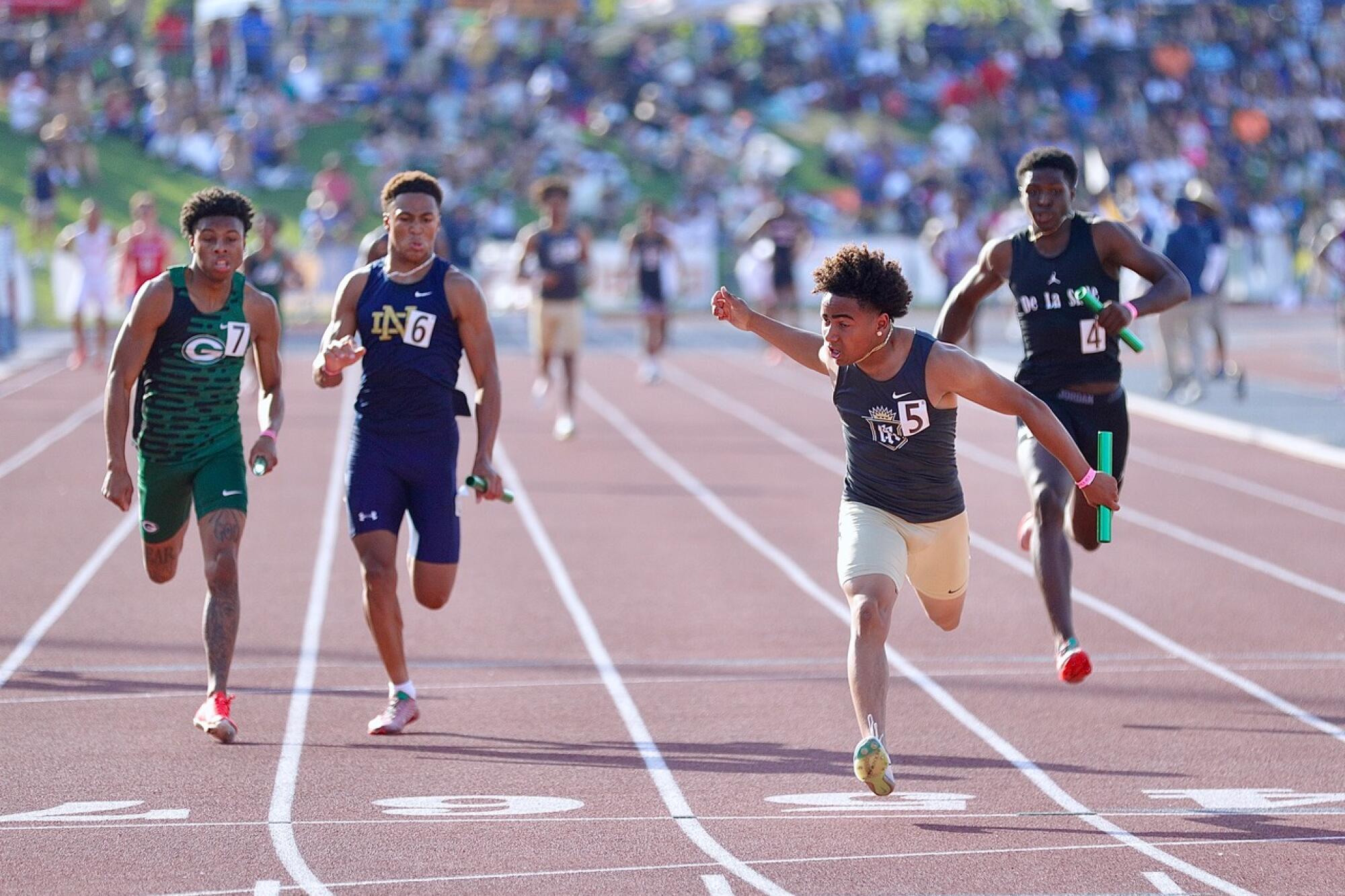 Servite's Jorden Wells stretches across the finish line to win the boys' 4X100-meter relay while competitors run behind him.