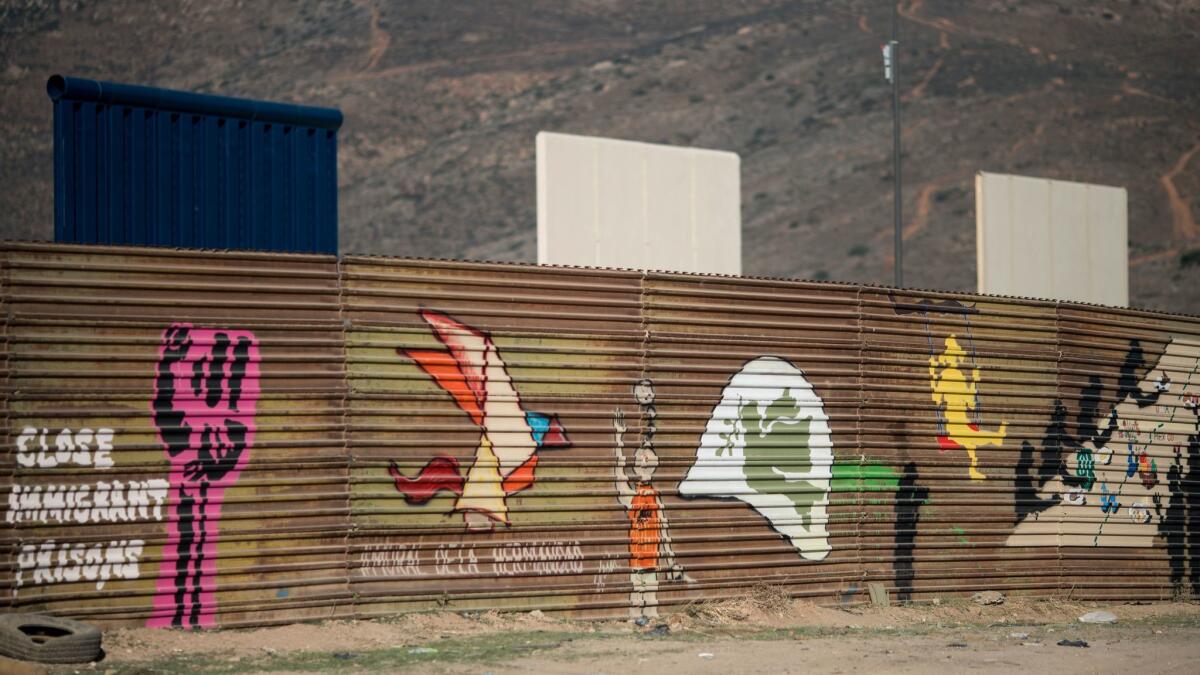 Murals decorate the current border fence in Tijuana. The new prototypes tower in the background.