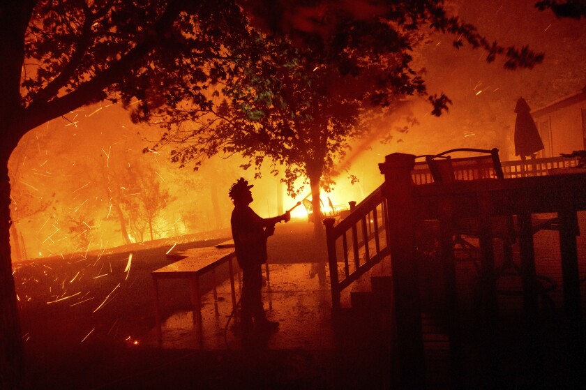 Matt Nichols sprays water on his home as fire nears and embers swirl through the air