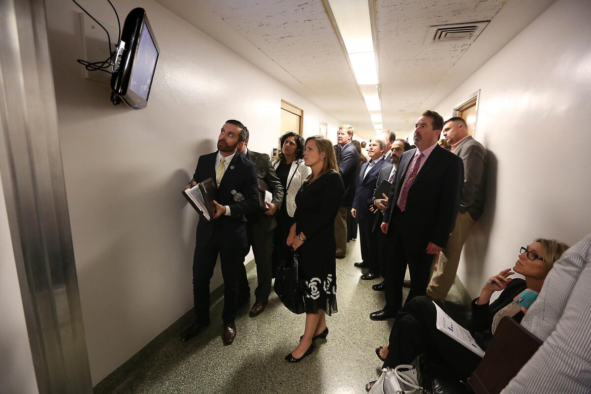 Lobbyists and advocates watch the action in the state Assembly on a television outside the Assembly Chambers at the Capitol in Sacramento in 2014. A panel decided Thursday to limit who lobbyists can bring to meetings with lawmakers.