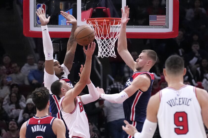 Chicago Bulls' Zach LaVine shorts between Washington Wizards' Daniel Gafford, left, and Kristaps Porzingis during the second half of an NBA basketball game Wednesday, Dec. 7, 2022, in Chicago. The Bulls won 115-111. (AP Photo/Charles Rex Arbogast)
