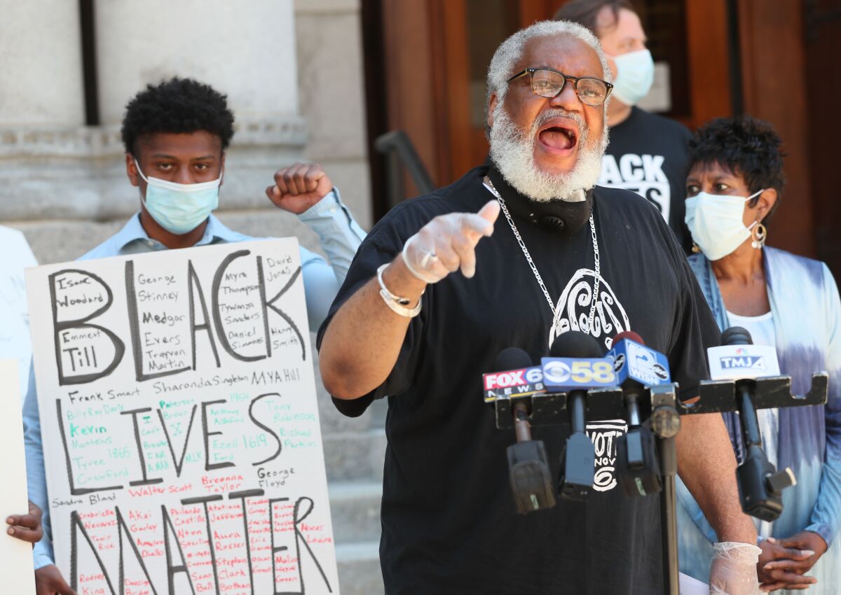 The Rev. Greg Lewis speaks next to a protester in a mask holding a Black Lives Matter poster.