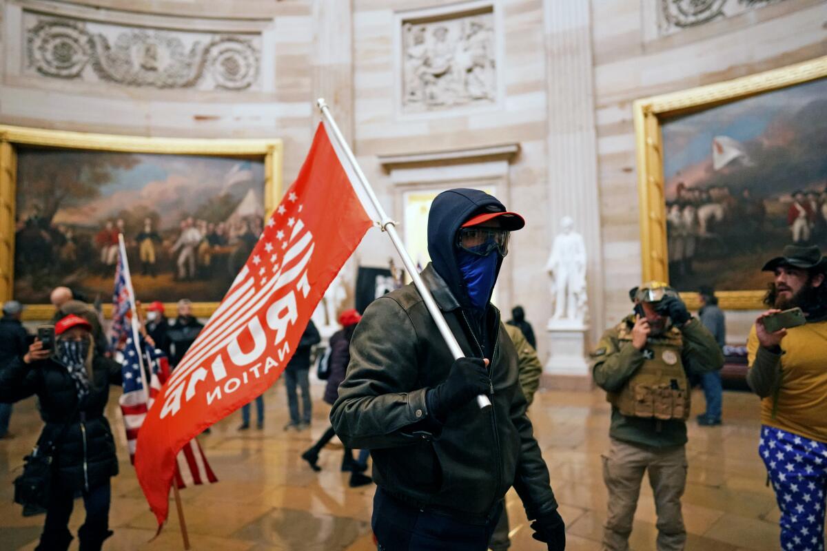 A masked protester carries a red flag reading "Trump Nation" in the Rotunda of the U.S. Capitol.