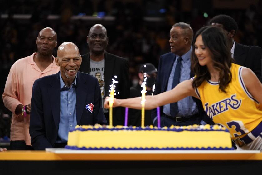 Kareem Abdul-Jabbar, front left, watches as candles are lit on his birthday cake during a celebration for his 75th birthday.