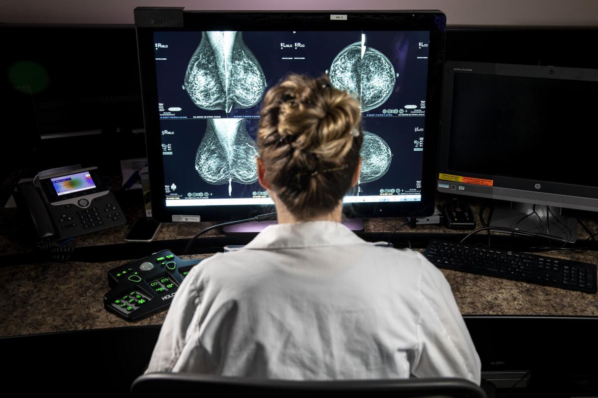 A person in a lab coat looks at a computer at a desk.