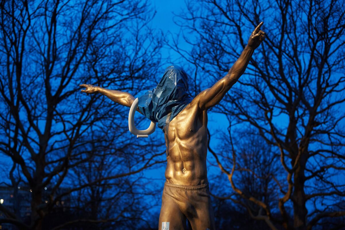 The statue of Zlatan Ibrahimovic covered in plastic and with a toilet seat on the arm.