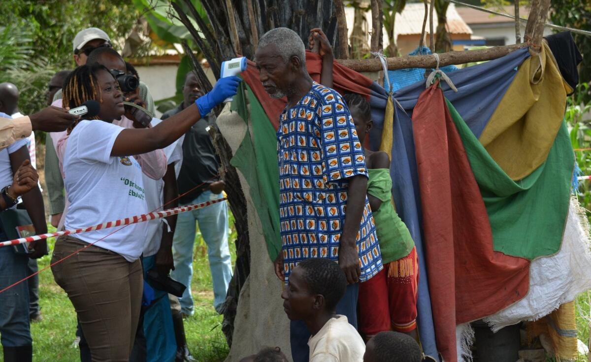 A medical worker near Monrovia, the Liberian capital, on Wednesday checks the temperature of a man who has been in quarantine since his daughter died from Ebola.