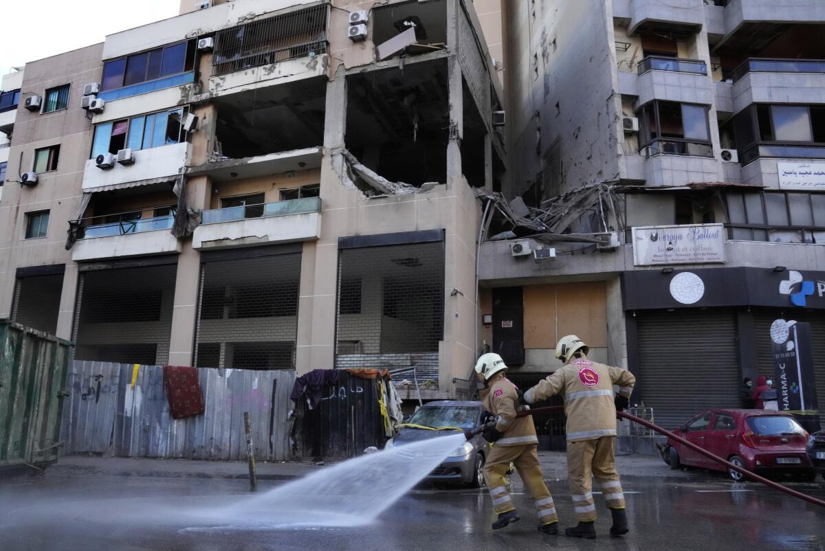 Civil defense workers hose off a street in front of a damaged apartment building.