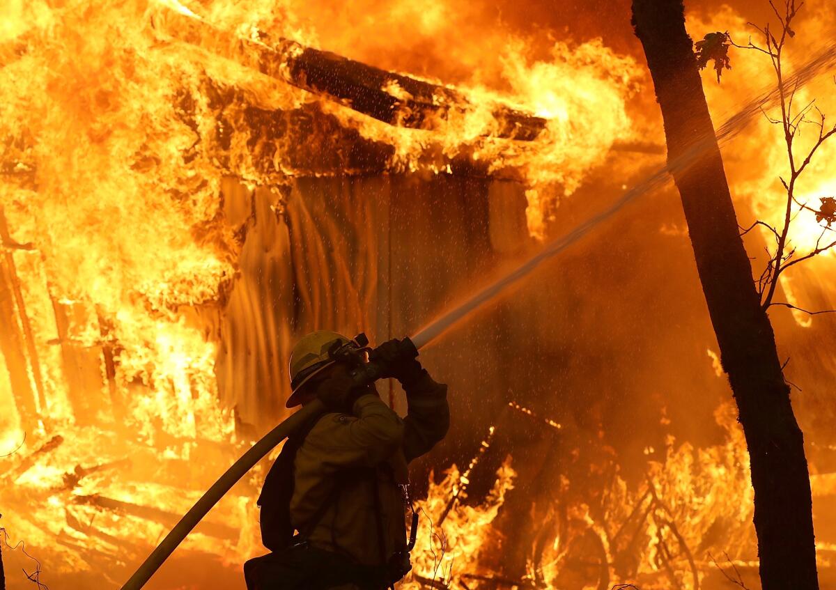 A Cal Fire firefighter sprays water around a burning home as the Camp fire moves through the area.