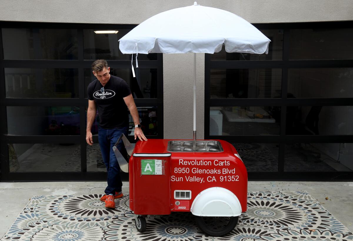 A person walks around a red cart with an umbrella.