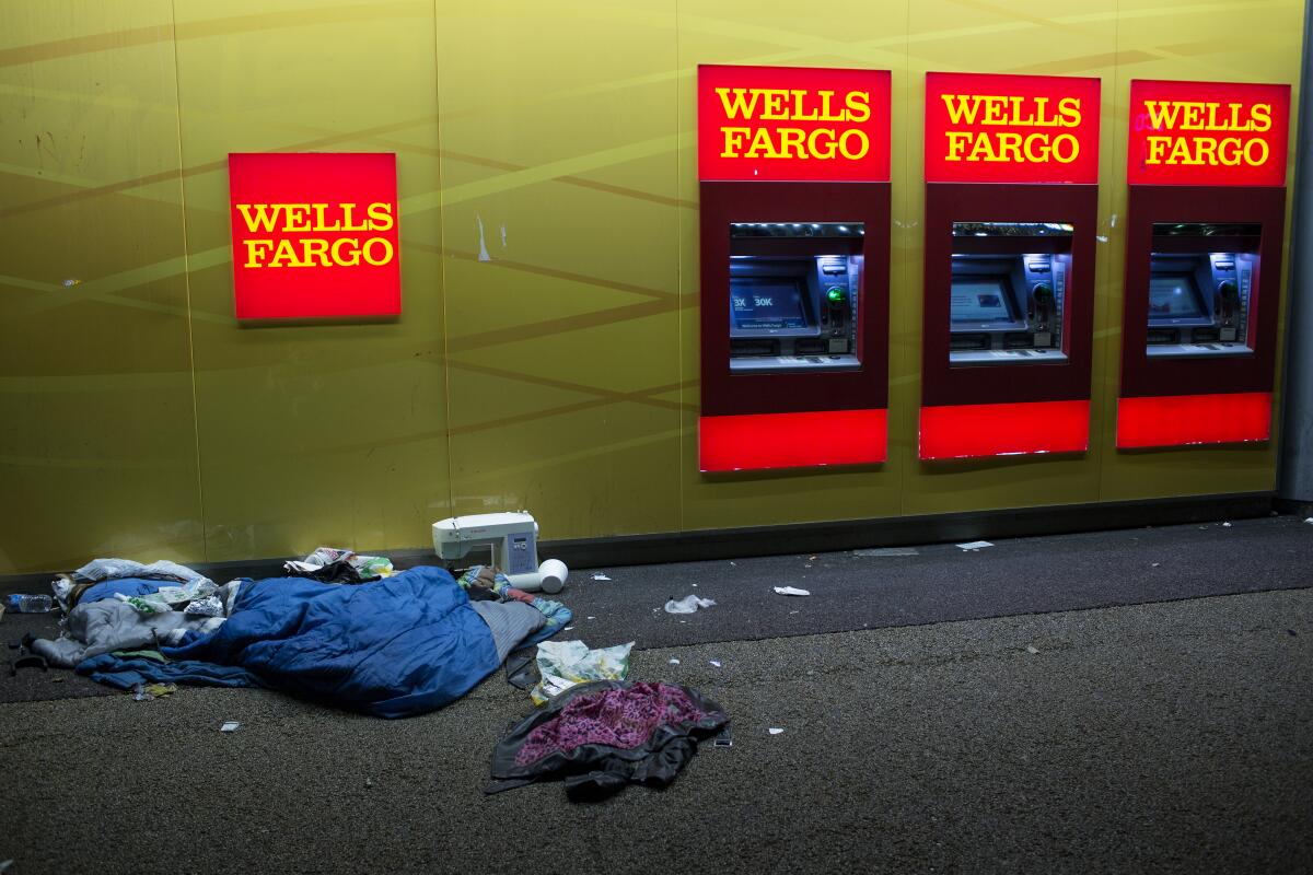 A person sleeps on the ground next to Wells Fargo ATM machines.