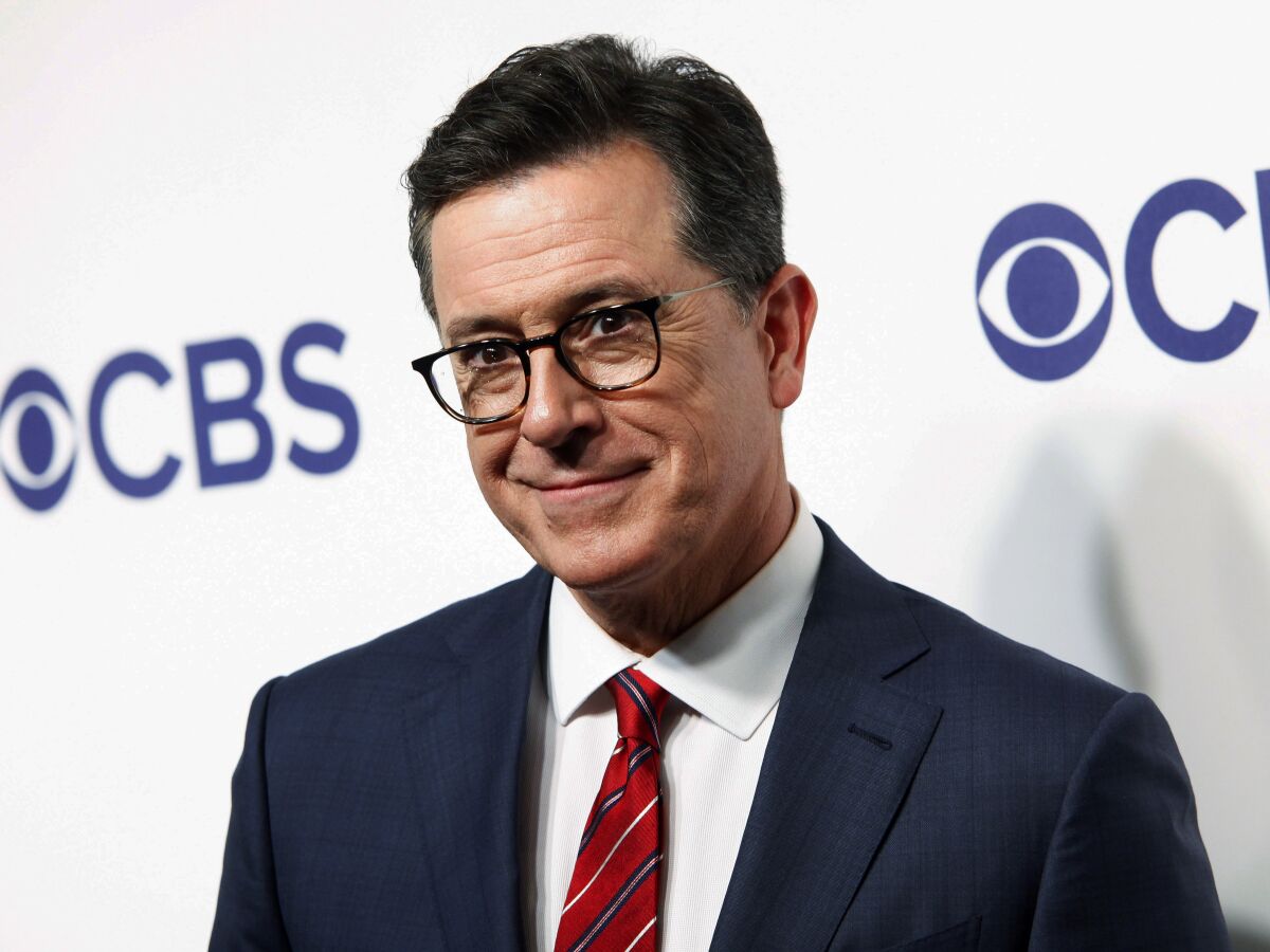 Stephen Colbert poses in a blue suit, white shirt and red tie