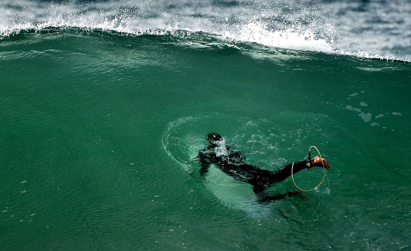 Una persona que practica surf se sumerge una ola en el rompeolas de Redondo Beach mientras que las olas altas golpean la costa sur de California.