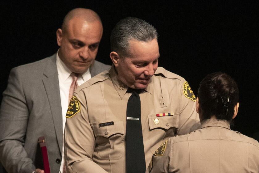 MONTEREY PARK, CA-DECEMBER 3, 2018: Los Angeles County Sheriff's Deputy Caren Carl Mandoyan, left, looks on as Alex Villanueva, the new Los Angeles County Sheriff, prepares to have his new badge pinned on him by his wife Vivian before he was sworn in during a ceremony at East Los Angeles College in Monterey Park on December 3, 2018. (Mel Melcon/Los Angeles Times)