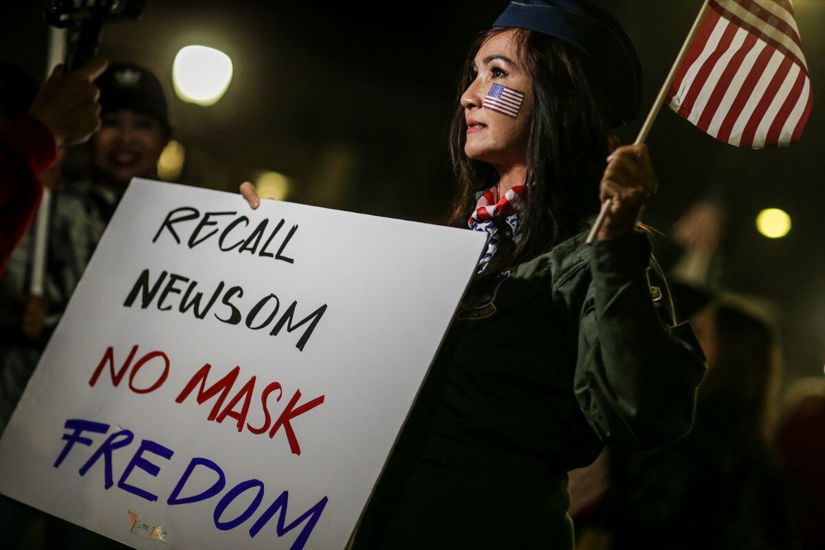 A woman holds a sign reading "Recall Newsom No Mask Fredom" [sic]
