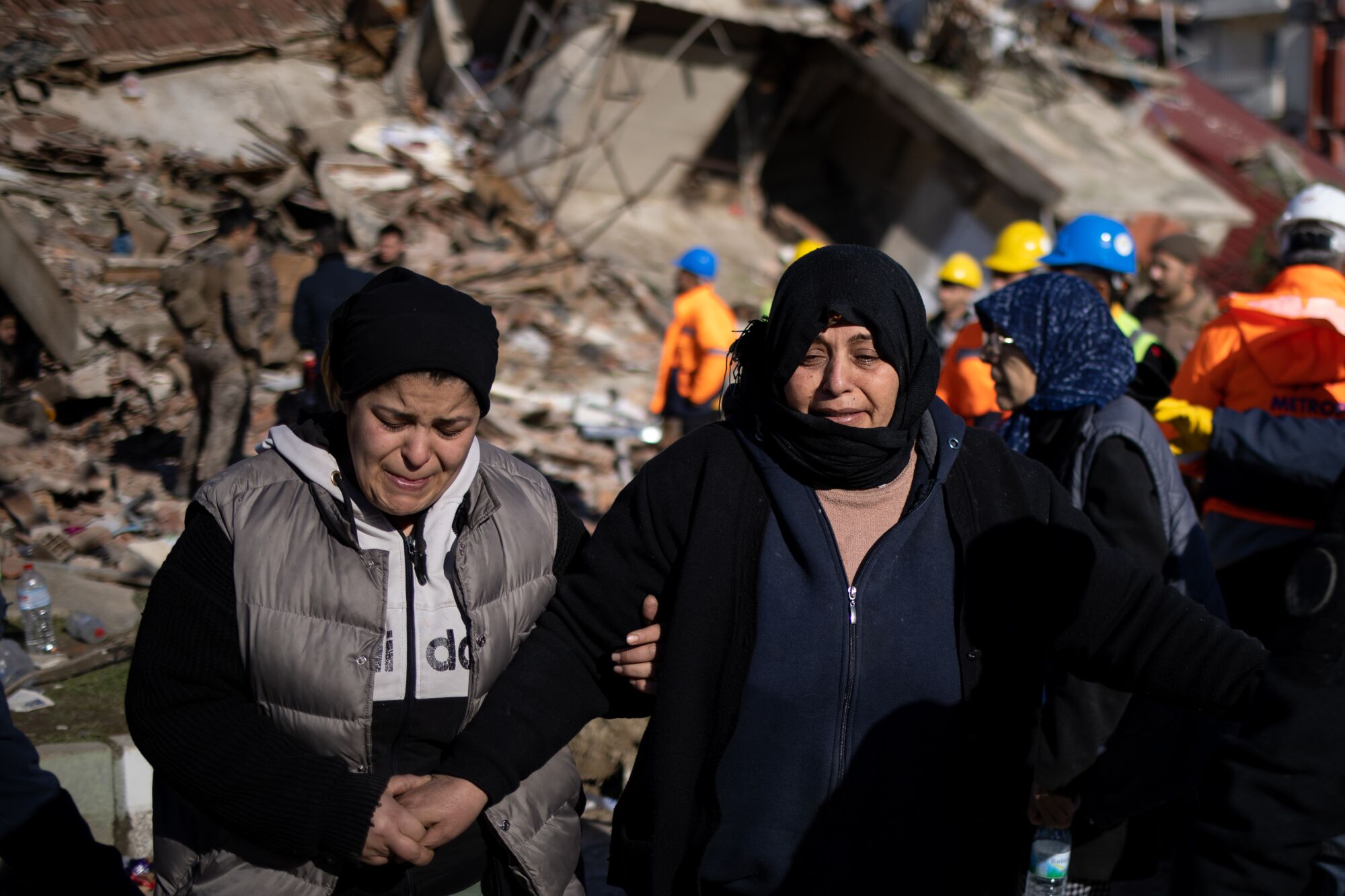 Women try to comfort each other as emergency services search through debris.