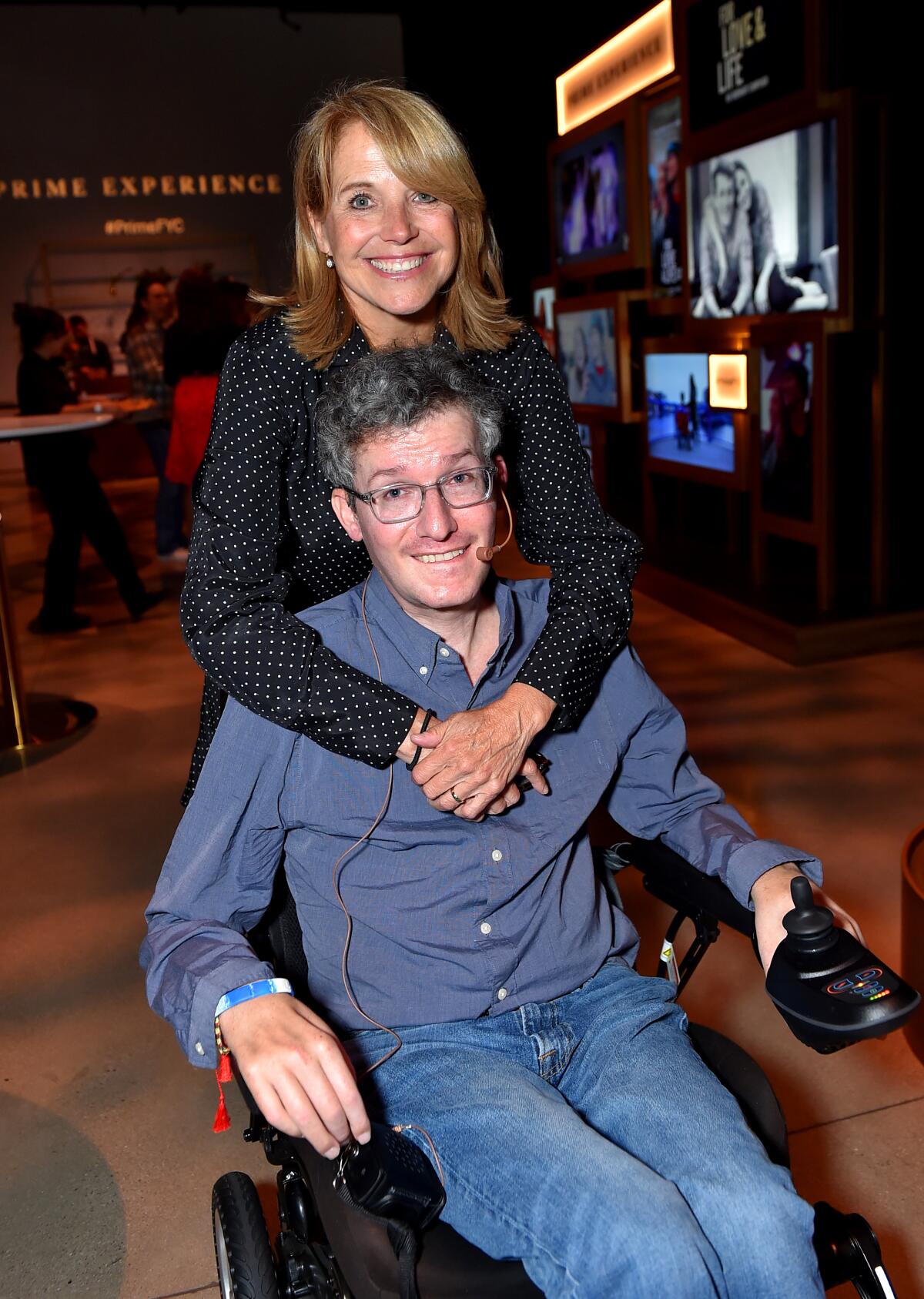Katie Couric stands behind Brian Wallach's wheelchair with her arms wrapped around him.