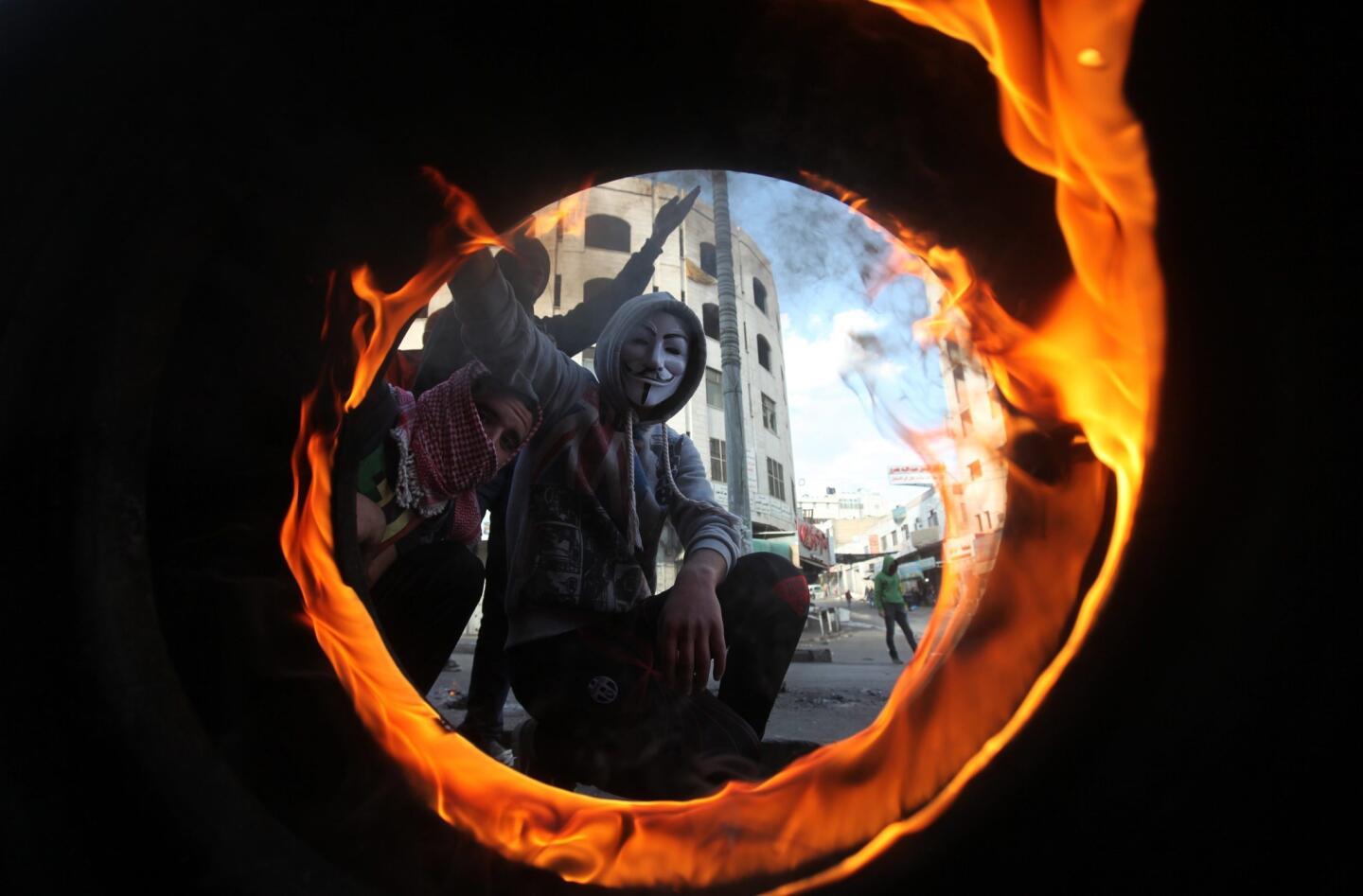 A Palestinian protester in a Guy Fawkes mask is seen through a burning tire during clashes with Israeli security forces after the funeral for a slain Palestinian in the West Bank city of Hebron.