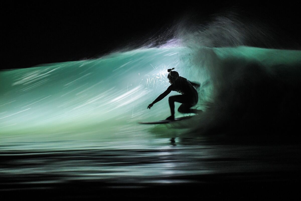A surfer using a waterproof headlamp rides a wave at the Cap Frehel beach in Plevenon, France.