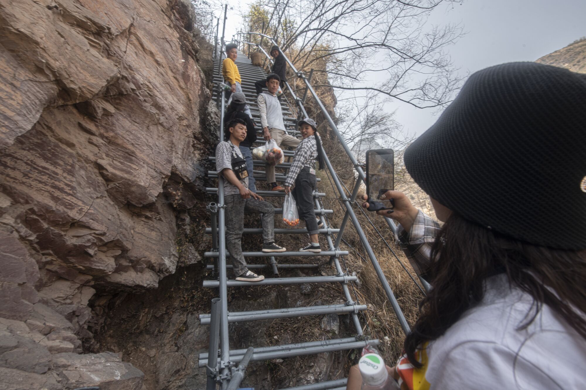 A young woman uses her cellphone to take a picture of young people standing on metal steps 